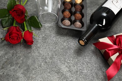 Photo of Red wine, chocolate truffles, gift box and roses on gray table, closeup. Space for text
