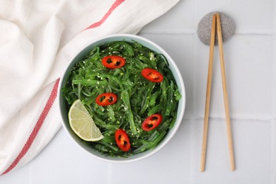 Photo of Tasty seaweed salad in bowl served on white tiled table, top view