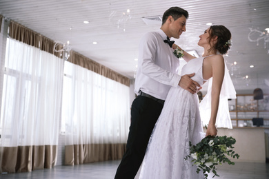 Happy newlywed couple dancing together in festive hall