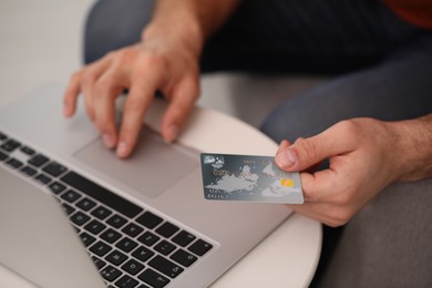 Photo of Man using laptop and credit card for online payment at table indoors, closeup