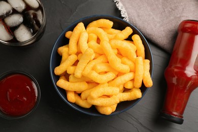 Photo of Bowl with crunchy cheesy corn snack, ketchup and refreshing drink on black table, flat lay
