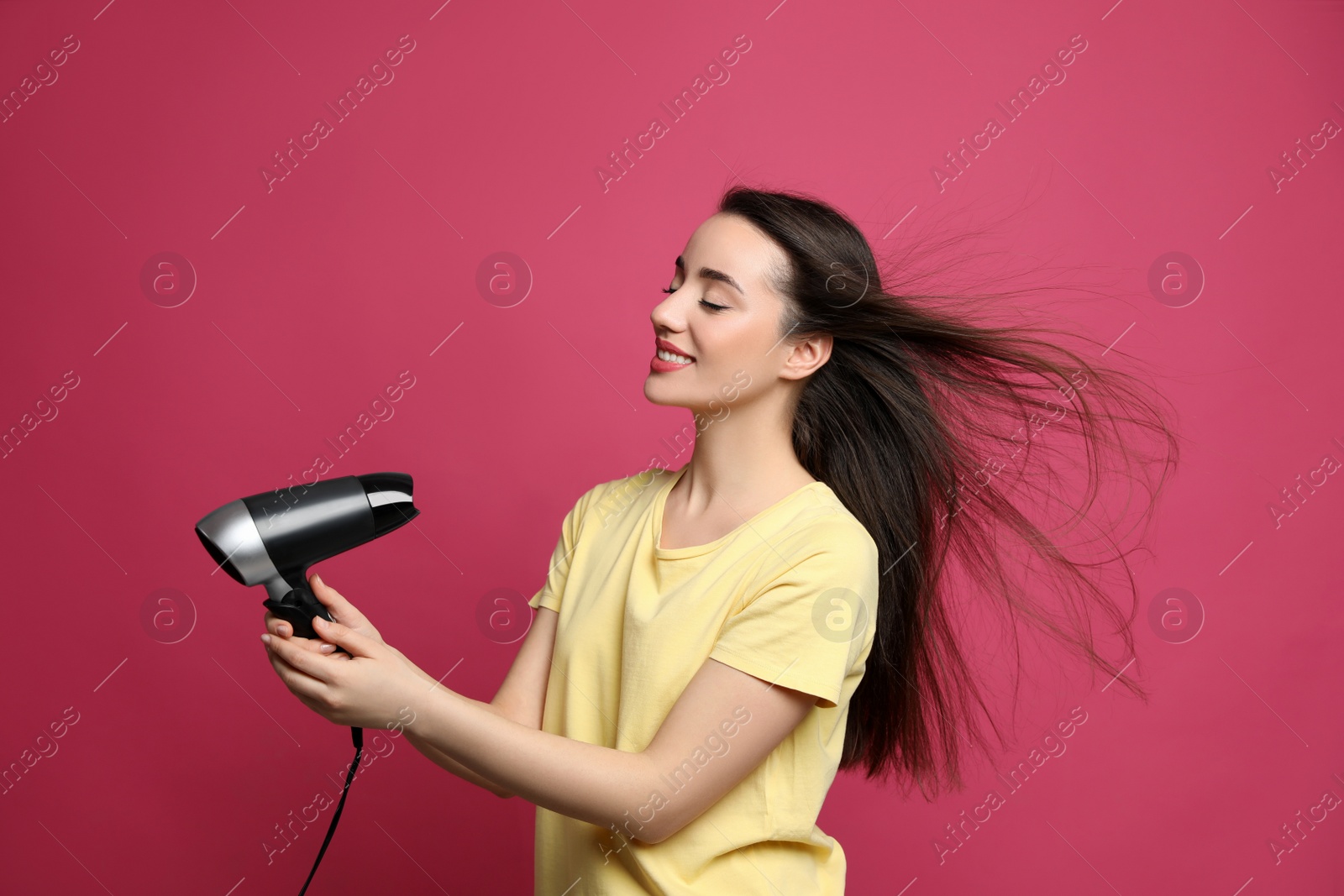 Photo of Beautiful young woman using hair dryer on pink background