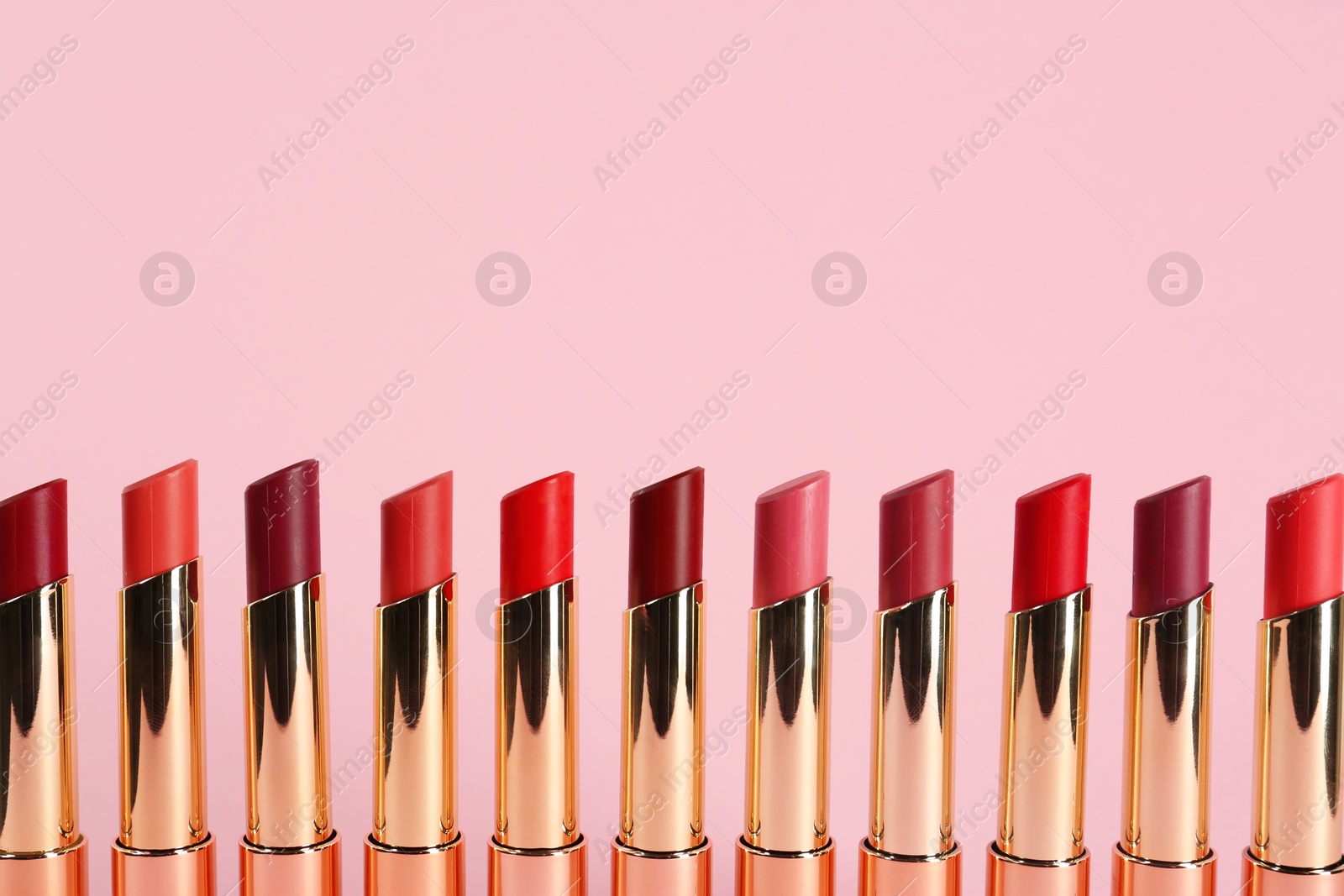Photo of Set of bright lipsticks in gold tubes on pink background, space for text