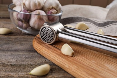 Photo of Garlic press and cloves on wooden table, closeup