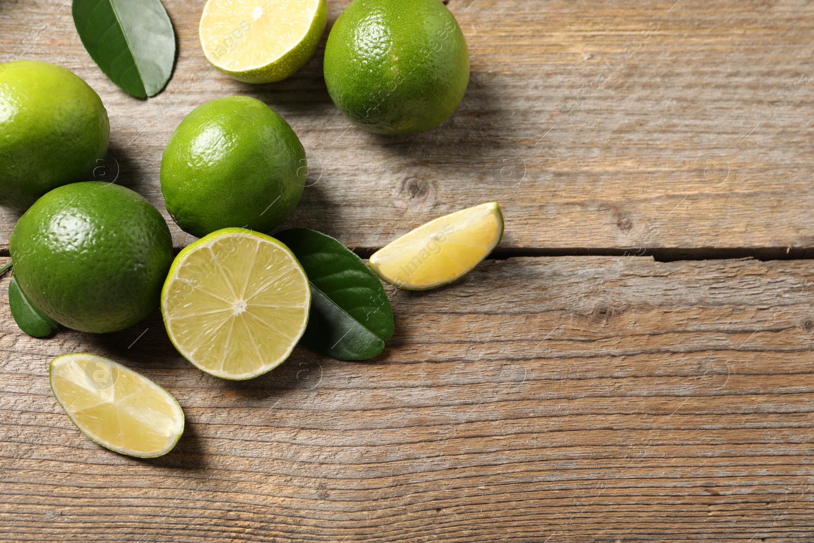 Photo of Fresh limes and green leaves on wooden table, flat lay. Space for text