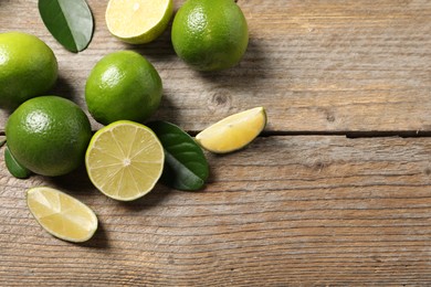 Photo of Fresh limes and green leaves on wooden table, flat lay. Space for text