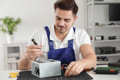 Male technician repairing power supply unit at table indoors