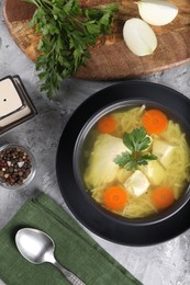 Photo of Tasty chicken soup with noodles, carrot and parsley in bowl served on grey textured table, flat lay