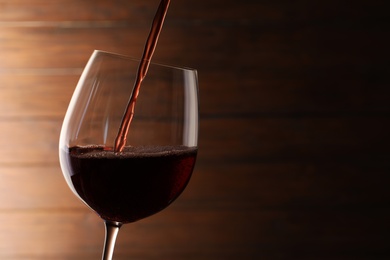 Pouring red wine into glass on blurred background. Space for text