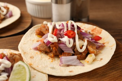 Photo of Delicious tacos with vegetables, meat and sauce on wooden table, closeup