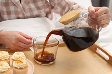 Photo of Woman pouring hot drink into cup in bed, closeup