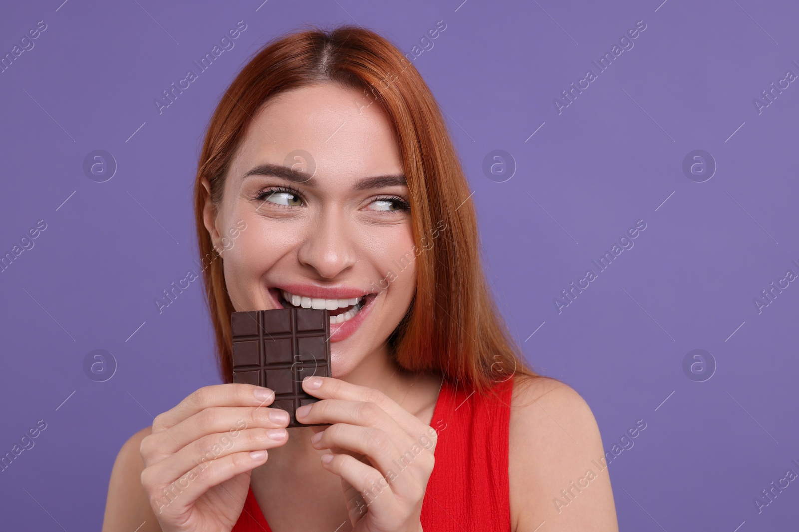 Photo of Young woman eating tasty chocolate on purple background, space for text