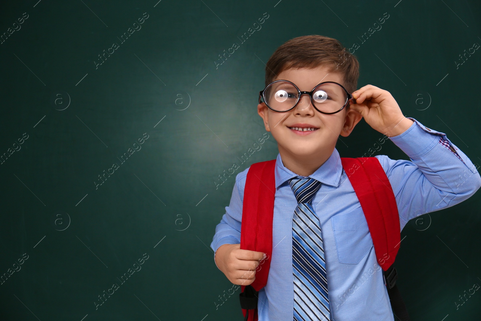 Photo of Cute little child wearing glasses near chalkboard, space for text. First time at school