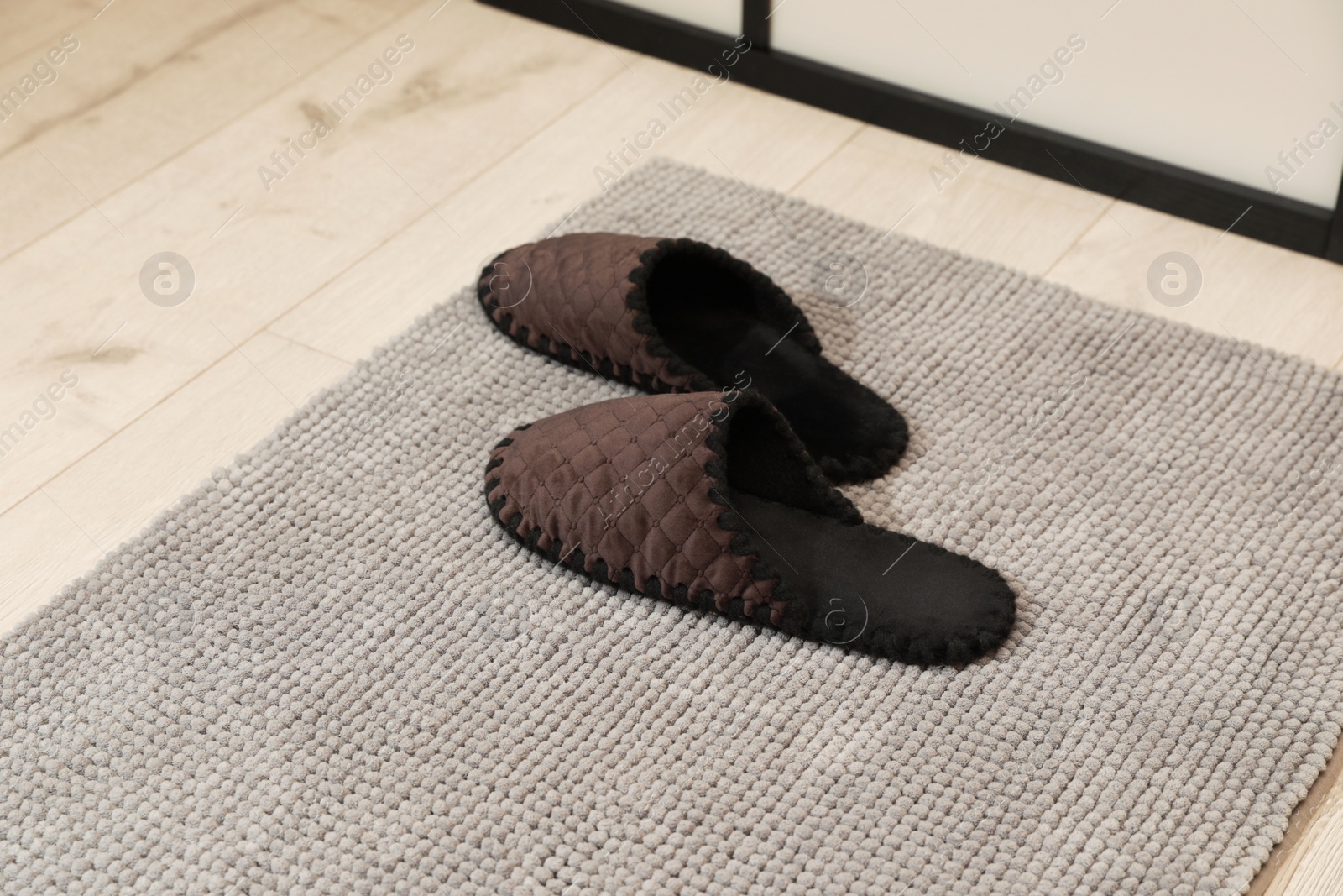 Photo of New grey bath mat with soft slippers on floor indoors