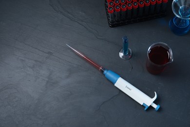 Photo of Laboratory analysis. Micropipette and different glassware on black table, flat lay. Space for text