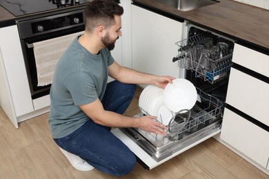 Photo of Man loading dishwasher with plates in kitchen