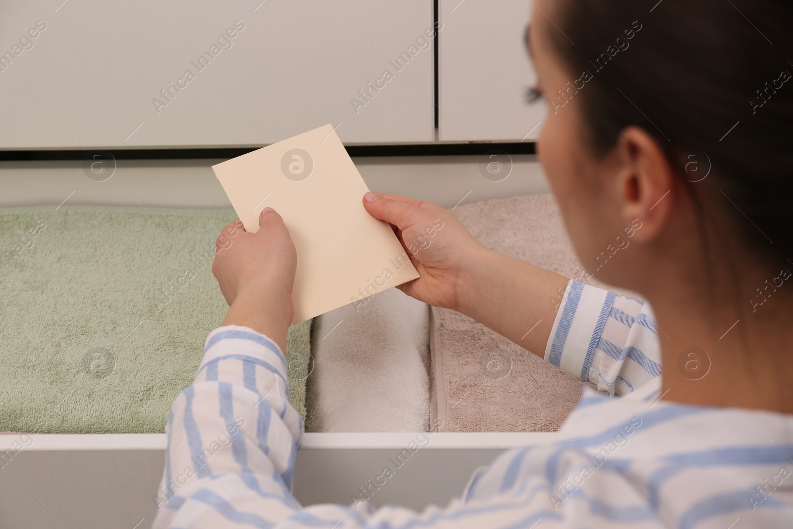 Photo of Woman putting scented sachet into drawer with towels