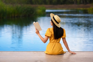 Woman reading book on pier near lake, back view