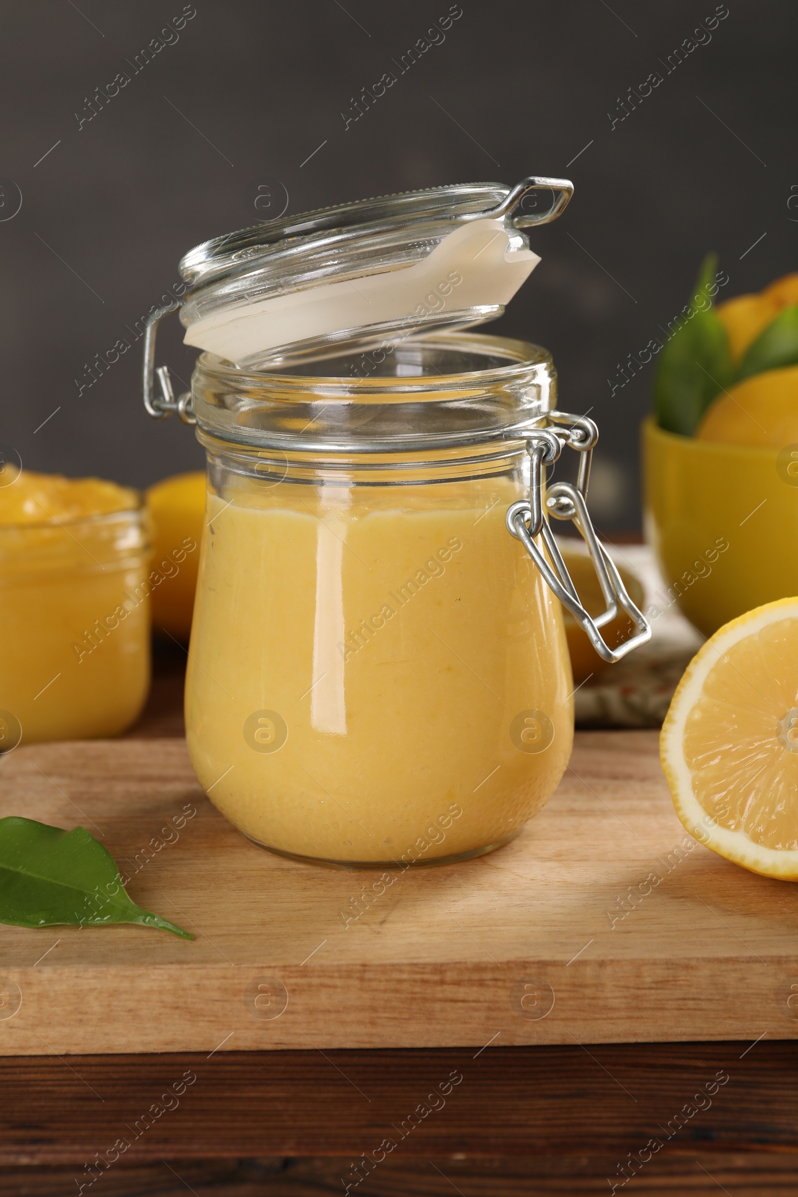 Photo of Delicious lemon curd in glass jars, fresh citrus fruit and green leaf on wooden table