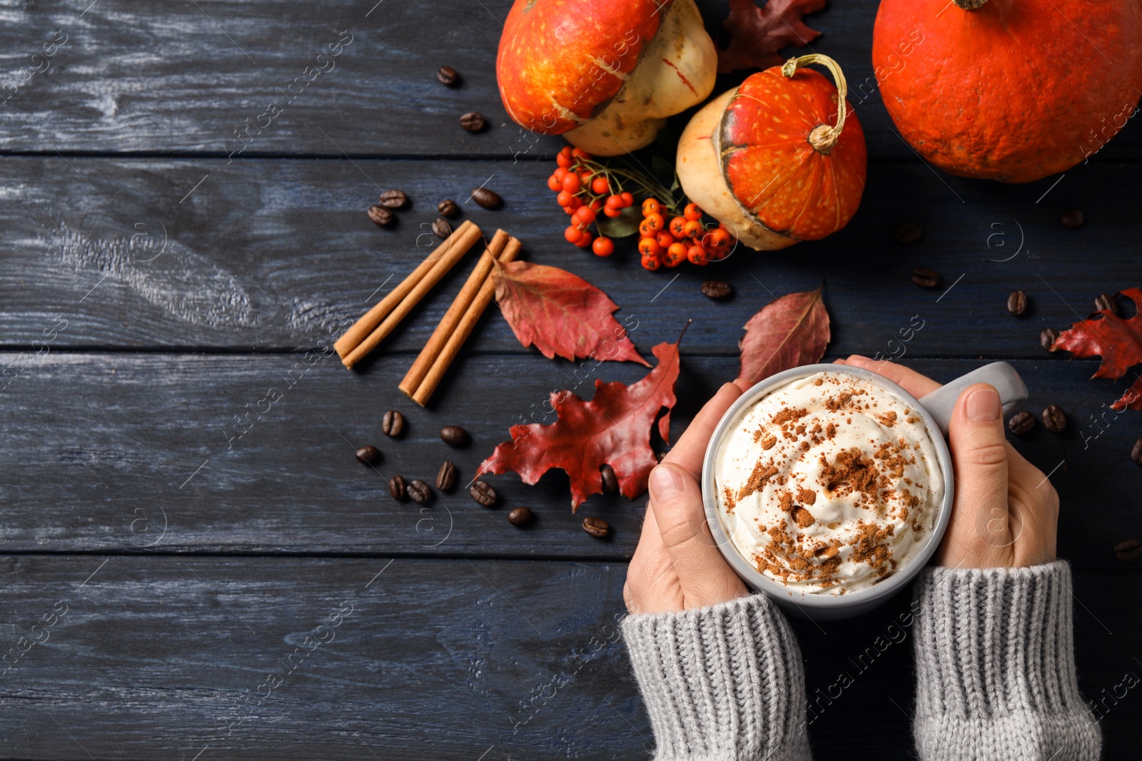 Photo of Woman with cup of tasty pumpkin spice latte at wooden table, top view. Space for text