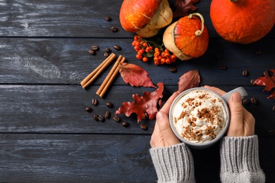 Photo of Woman with cup of tasty pumpkin spice latte at wooden table, top view. Space for text