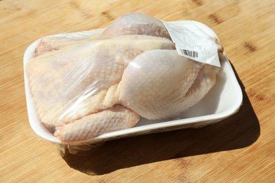 Photo of Fresh raw whole chicken in plastic container on wooden table