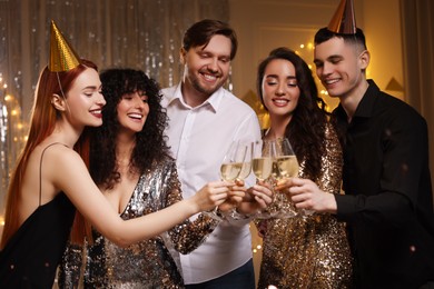 Happy friends clinking glasses of sparkling wine at birthday party indoors
