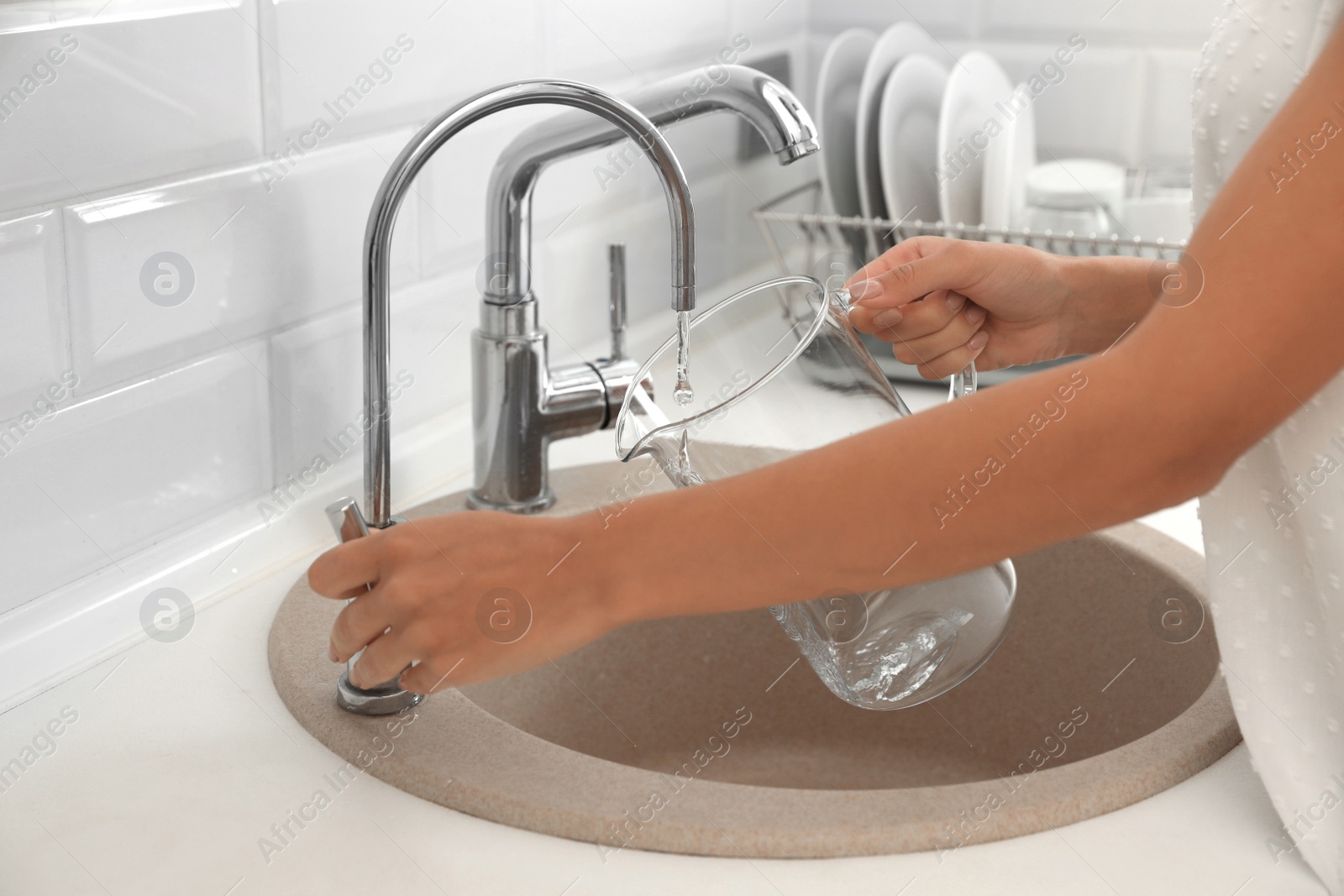 Photo of Woman pouring water into glass jug in kitchen, closeup