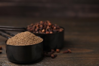 Photo of Aromatic clove powder and dried buds in scoops on wooden table, closeup. Space for text