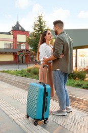 Photo of Long-distance relationship. Beautiful young couple with suitcase at railway station outdoors