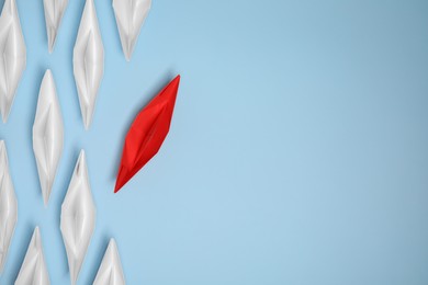 Photo of Red paper boat floating away from others on light blue background, flat lay with space for text. Uniqueness concept