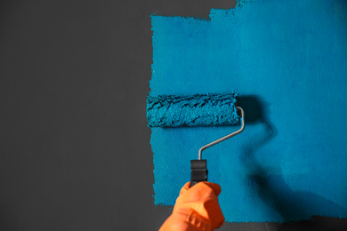 Photo of Woman painting grey wall with blue dye, closeup