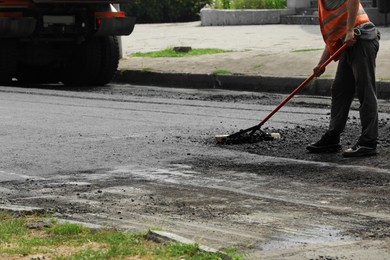 Photo of Worker laying new asphalt on city street, closeup. Road repair service