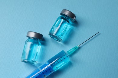 Photo of Disposable syringe with needle and vials on light blue background, flat lay