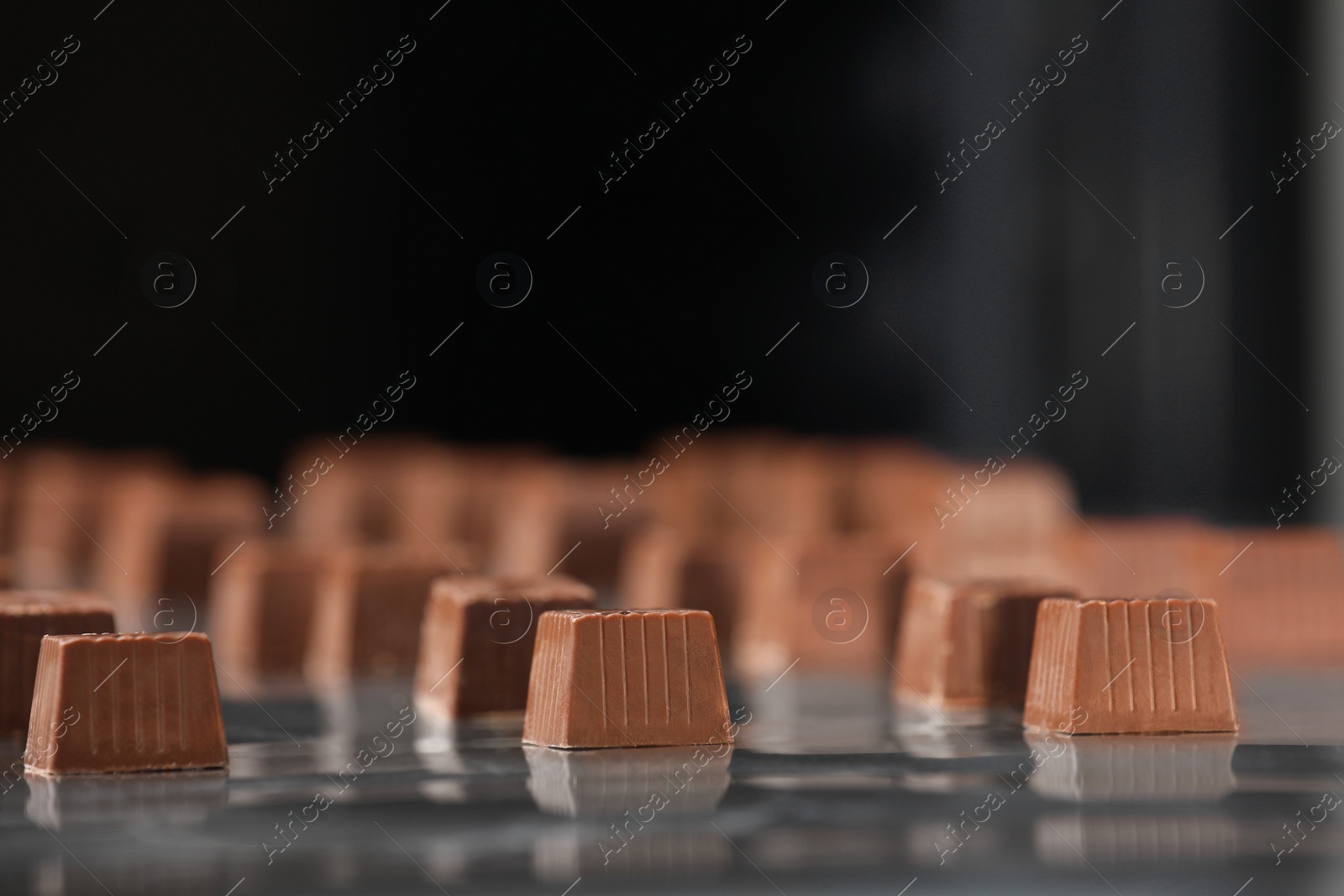 Photo of Many delicious chocolate candies on production line, closeup