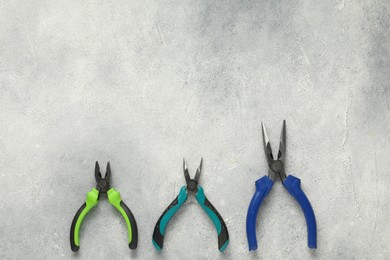 Photo of Different pliers on grey textured table, flat lay. Space for text