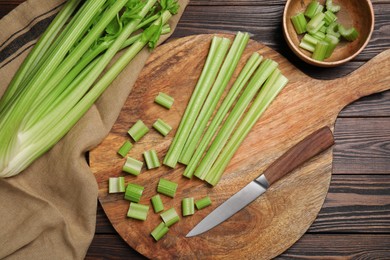 Photo of Board with fresh cut celery stalks and bunch on wooden table, flat lay