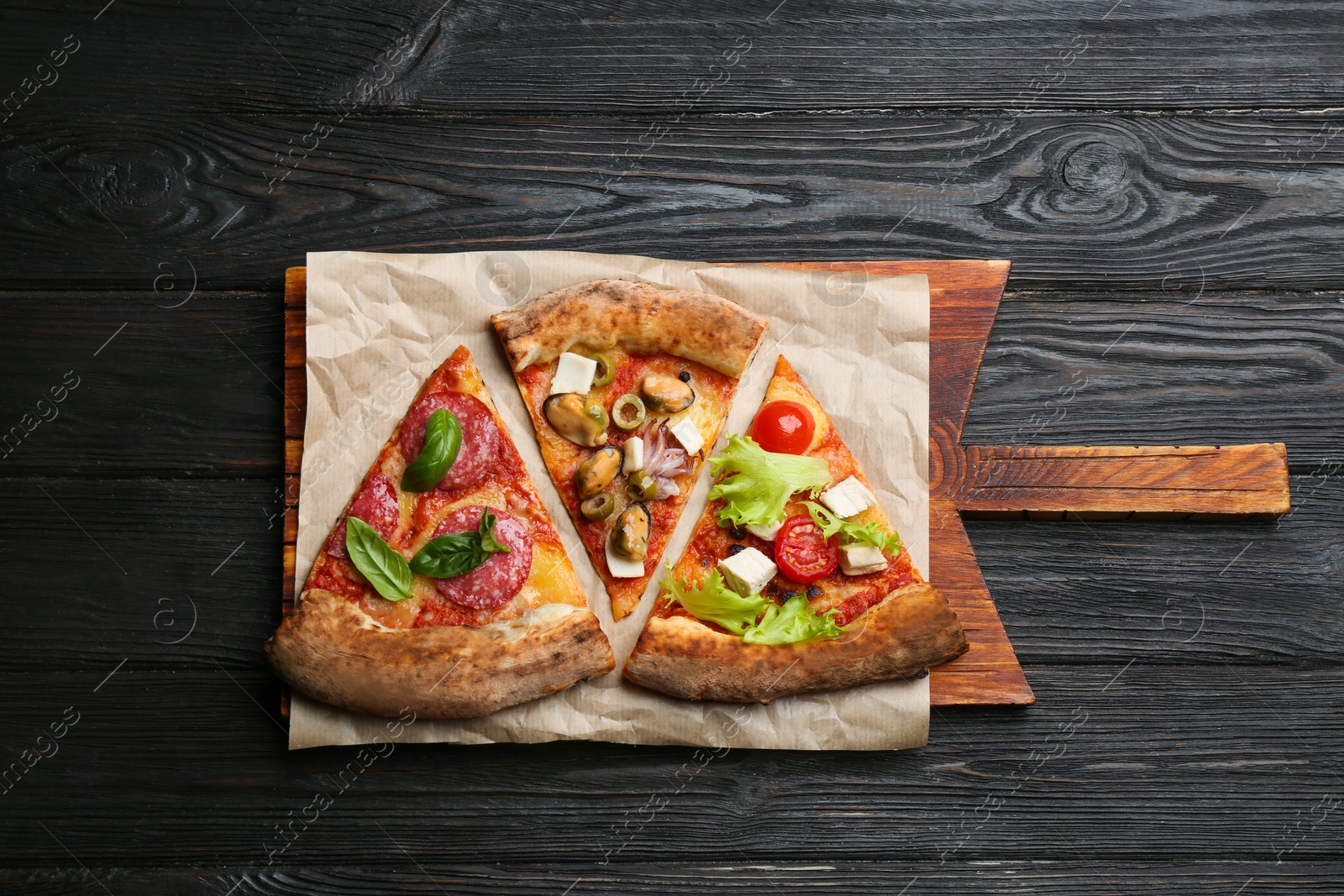 Photo of Slices of different delicious pizzas on black wooden table, top view