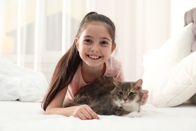 Cute little girl with cat lying on bed at home. First pet