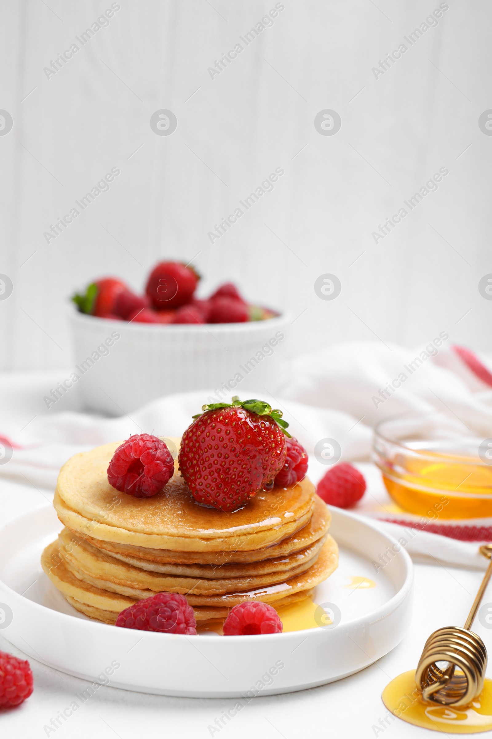 Photo of Tasty pancakes with fresh berries and honey on white table