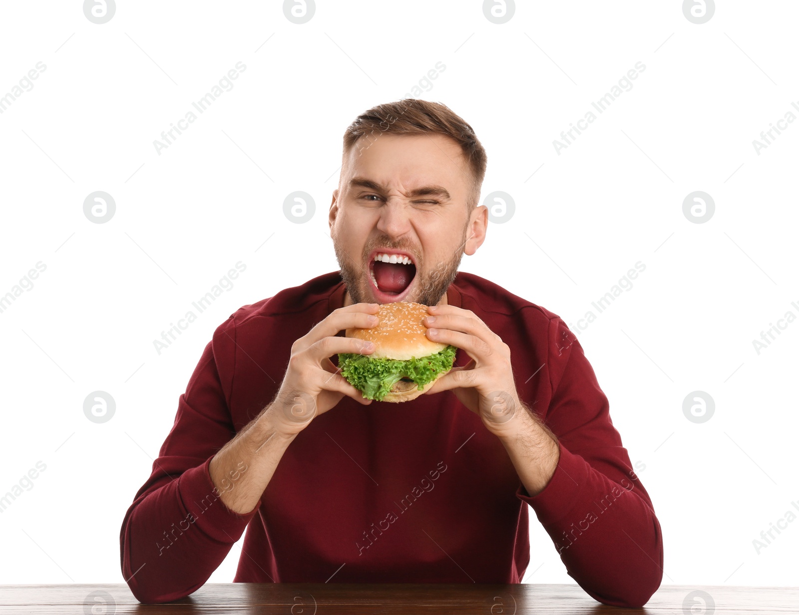 Photo of Young man eating tasty burger at table on white background