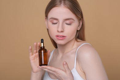 Beautiful young woman with bottle of essential oil on brown background