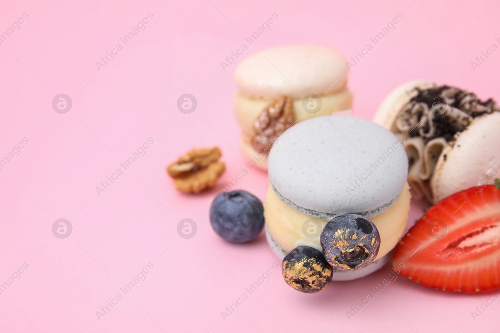 Photo of Delicious sweet macarons, berries and walnuts on pink background, closeup. Space for text