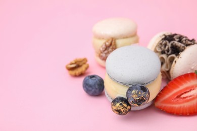 Delicious sweet macarons, berries and walnuts on pink background, closeup. Space for text