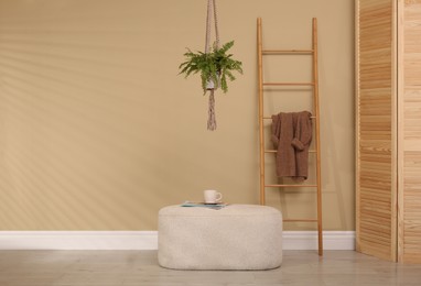 Photo of Stylish room interior with comfortable pouf and ladder near beige wall
