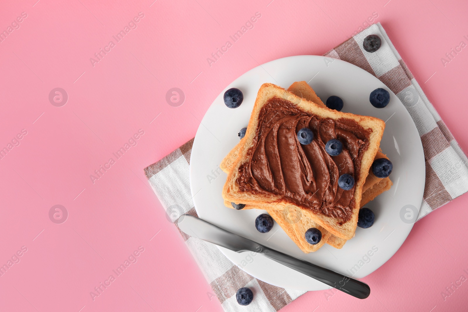 Photo of Tasty toast with chocolate paste and blueberries on pink table, top view. Space for text