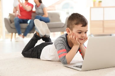 Photo of Boy with laptop lying on carpet near his family at home