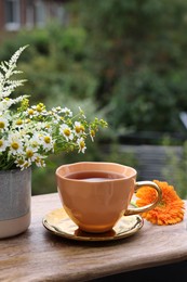 Cup of delicious chamomile tea and fresh flowers outdoors