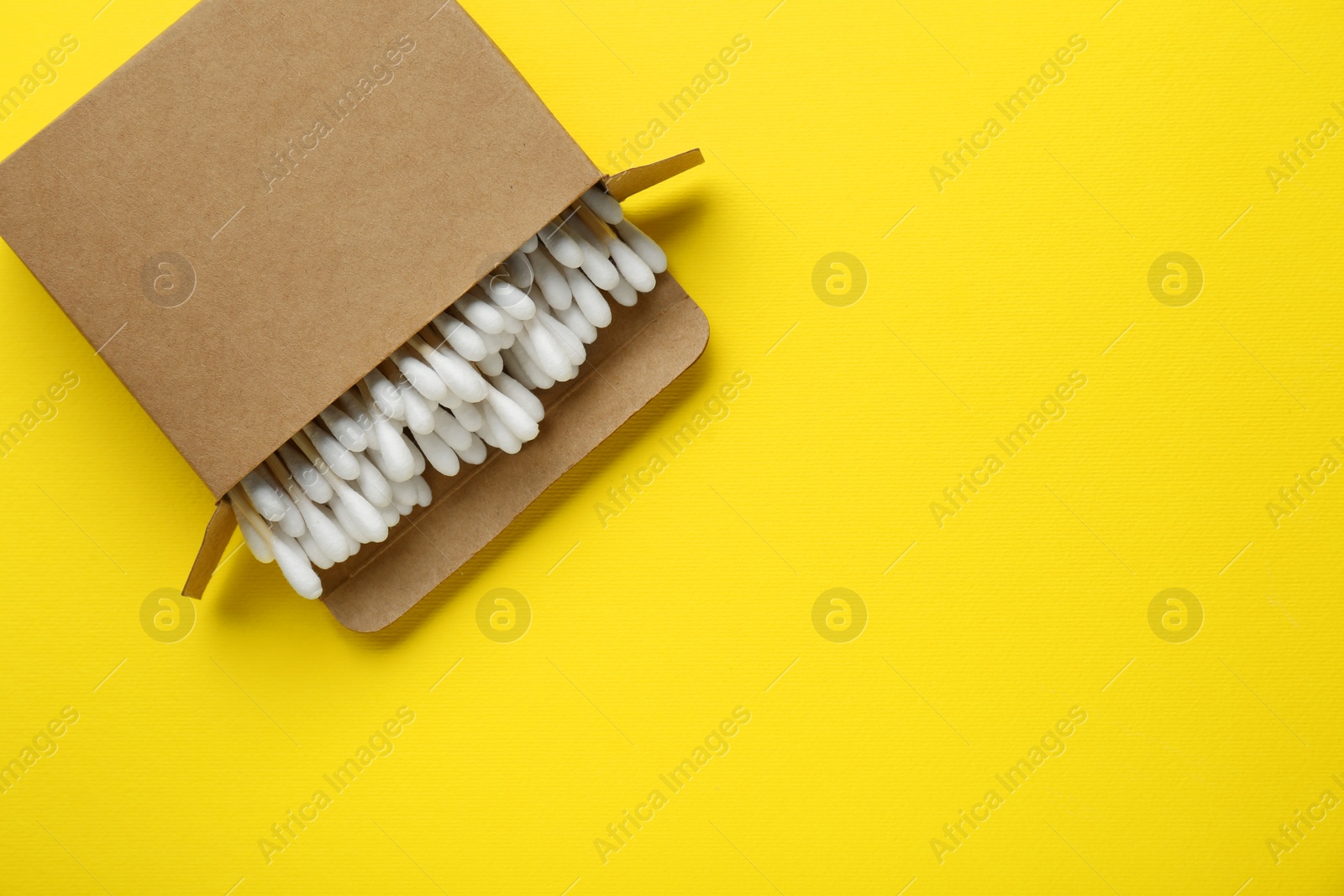 Photo of Cardboard box with cotton buds on yellow background, top view. Space for text