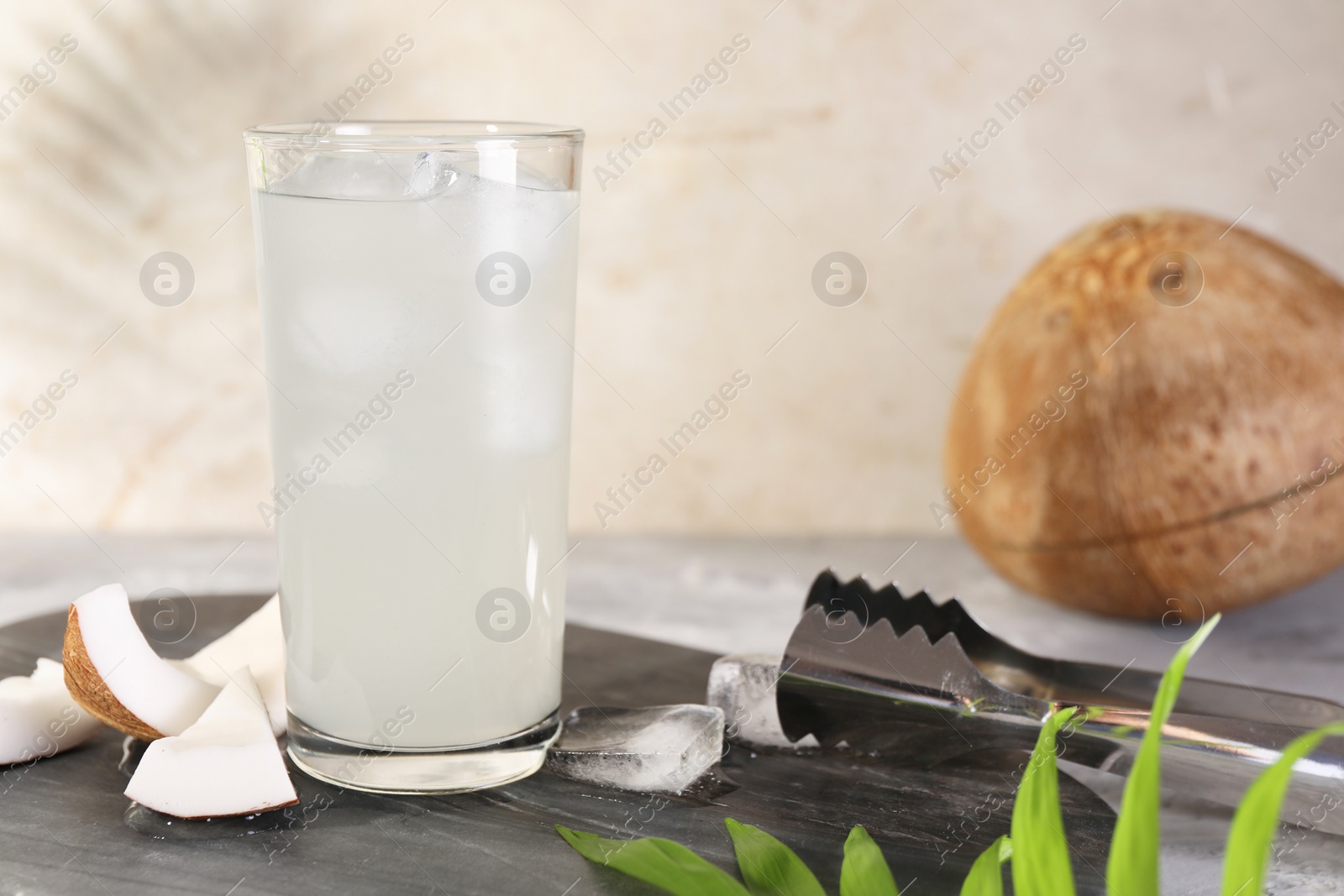 Photo of Glass of coconut water, ice cubes and nuts on grey table